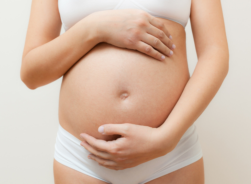 Midsection Of Pregnant Woman Touching Abdomen While Standing Against White Background